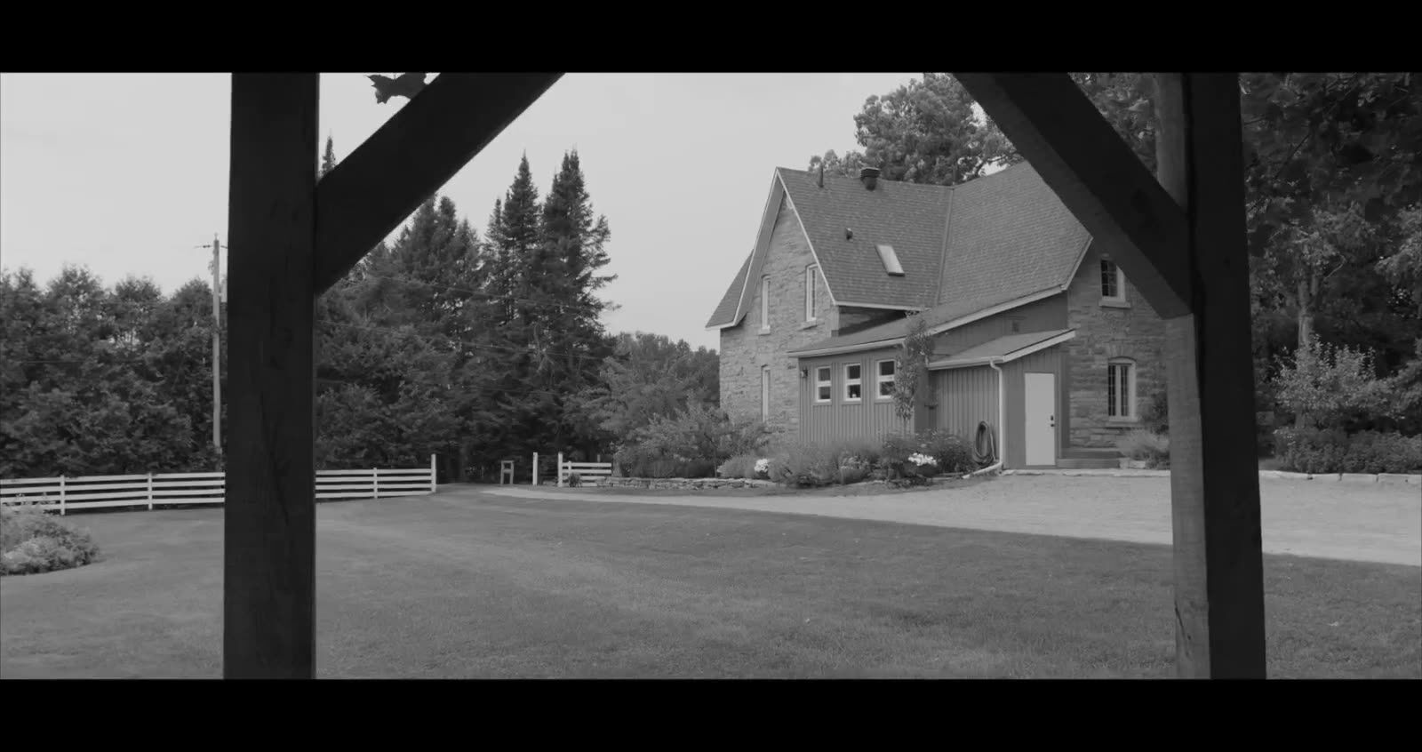 A stone farmhouse framed through a wooden barn beam
